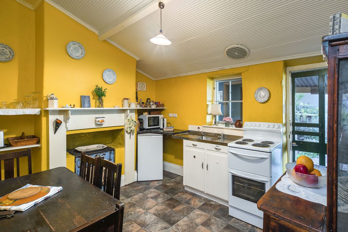 The cottage kitchen with mustard walls, an oven, kettle, fruit bowl and dining table