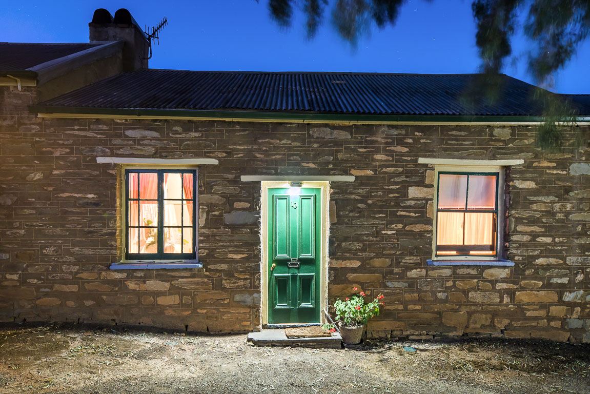 A lit cottage window and green front door at dusk